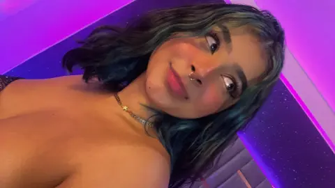 Young woman with blue hair and nose ring smiling in moody purple neon lighting.