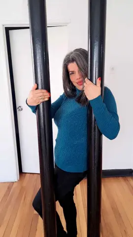 Smiling woman in a teal turtleneck sweater posing between black pillars in a bright room.