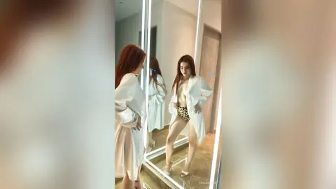 Redheaded woman in a white oversized shirt and leopard print briefs posing in a modern bathroom mirror.