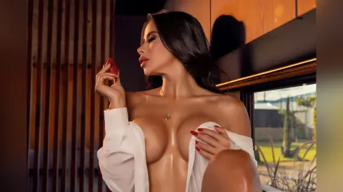 Glamorous woman in a white shirt posing sensually in a modern, sunlit room.