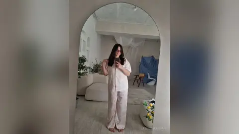 LateshaKaspar poses in a mirror wearing a light pink button-up shirt and matching wide-leg pajama pants in a bright, white room.