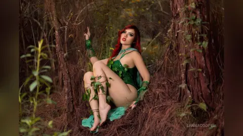 LannaCooper poses in a green lace bodysuit while sitting among thick vines and forest brush.