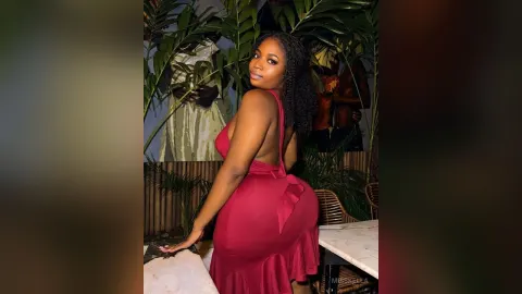 Misskella — Misskella poses in a tight red dress while looking back over her shoulder in a tropical setting.