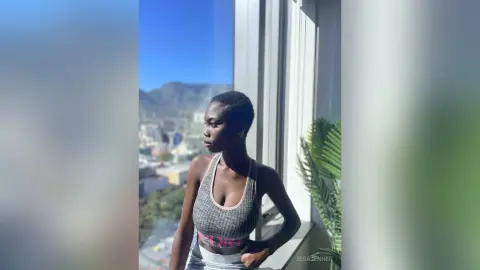 Thoughtful young woman in a grey sports bra relaxing by a bright window with a scenic mountain view.