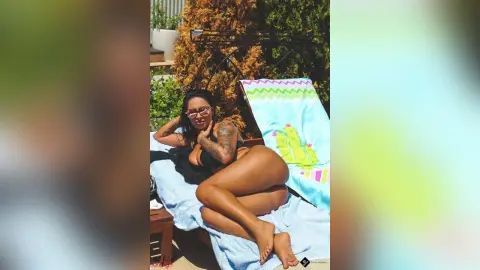 DeeaAnderson reclines naked on a blue towel outdoors, showing her bare buttocks and tanned skin.