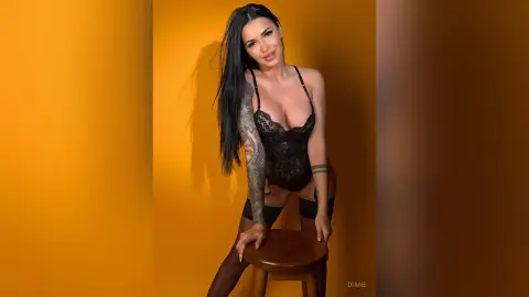 Smiling woman in black lace bodysuit and stockings posing against a vibrant yellow studio background.