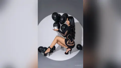 Elegant woman in a black cutout dress holding a drink amidst black balloons for a chic celebratory mood.