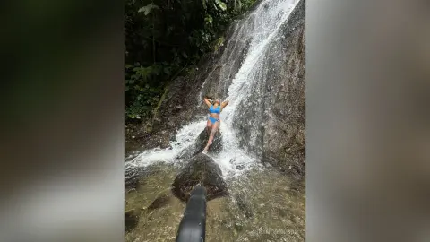 Adventurous woman in a blue bikini standing by a cascading jungle waterfall in a lush tropical forest.