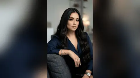 Elegant woman in a navy blue silk blouse posing with a confident expression in a modern indoor setting.