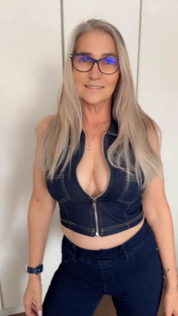 SexyScarlett22 poses with her long blonde hair, wearing a low-cut denim vest that shows deep cleavage.