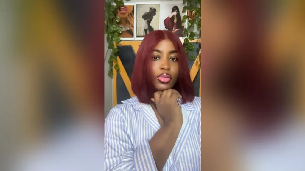 ZaraLure — ZaraLure poses with her hand under her chin, wearing a blue and white striped button-down shirt.