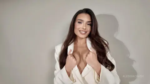 Smiling young woman in a white blazer posing against a neutral studio background.