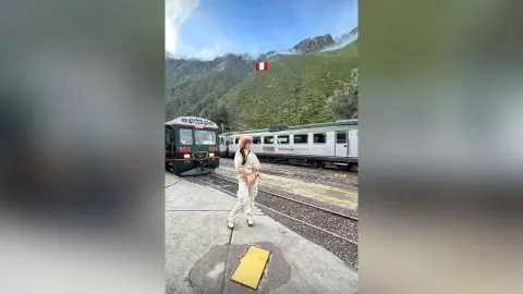 Stylish woman in white winter outfit standing by a train in the scenic Peruvian mountains.