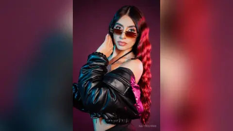 Stylish woman in a black leather jacket and sunglasses posing against a moody pink and purple studio background.