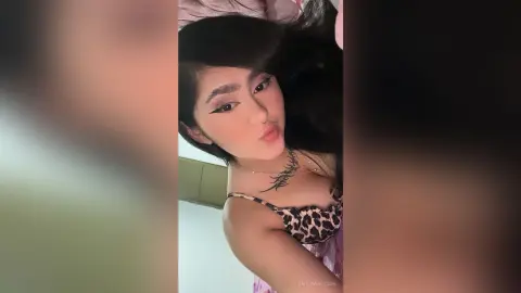 Young woman with dark hair wearing a leopard print camisole making a playful pouty face indoors.
