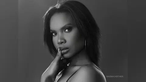 Elegant Black woman in a dark studio setting posing for a moody black and white portrait.