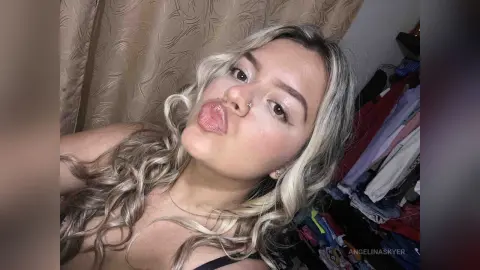 Blonde woman with wavy hair making a playful kissy face in a cozy indoor setting.