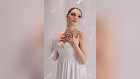 Elegant woman in a white lace wedding dress posing gracefully against a soft ethereal backdrop.