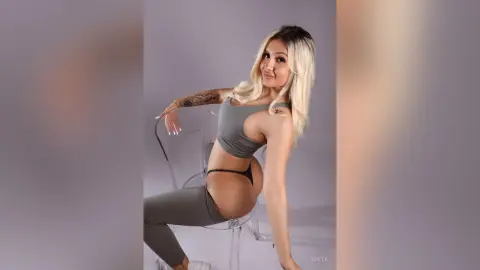 Anita poses sitting on a clear chair wearing a grey sports bra and matching leggings, showing her side profile and tattoo.