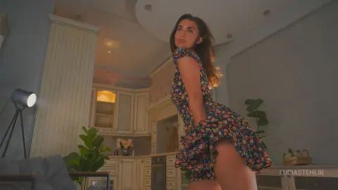 Young woman in a floral print summer dress posing in a bright, modern kitchen setting.