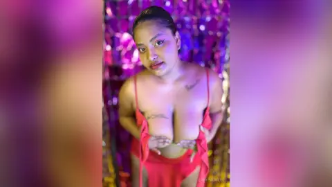 Beautiful woman in a red slip dress posing against a shimmering purple tinsel background.