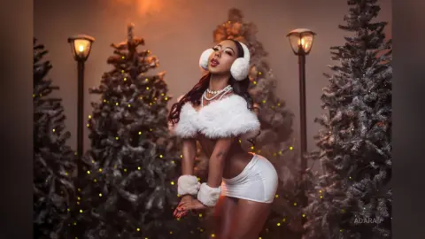 Glamorous woman in white faux fur outfit posing amidst festive Christmas trees and warm glowing lanterns.