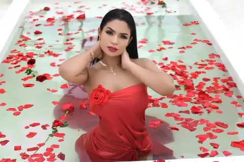 Emilycurtiis poses in a white tub filled with water and red rose petals, wearing a strapless red dress.
