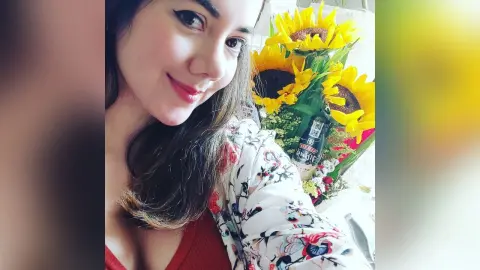 Smiling young woman in a floral print blouse holding a bright bouquet of sunflowers in a sunny setting.