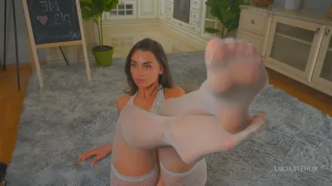 Young woman in white lace lingerie relaxing on a grey shag rug in a bright, cozy living room.