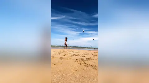 Woman in a white summer dress walking on a sunny beach under a blue sky.