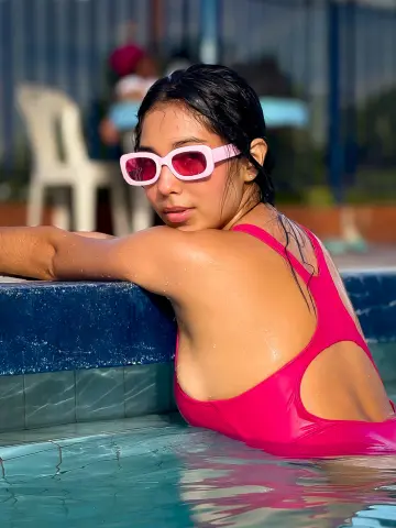 Young woman in pink sunglasses and swimsuit relaxing in a sunny outdoor swimming pool.