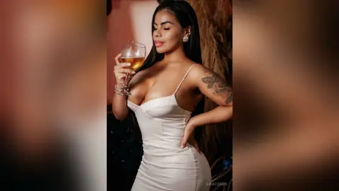 Elegant woman in a white satin dress holding a glass of wine in a moody, sophisticated indoor setting.