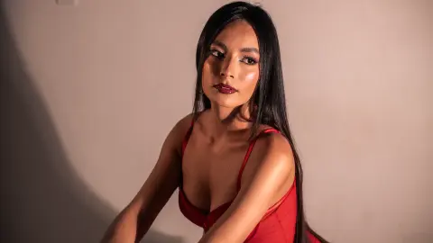 Elegant woman in a red dress posing against a neutral studio background with dramatic lighting.