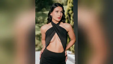 Elegant woman in a black halter neck cutout dress posing outdoors in a lush garden setting.