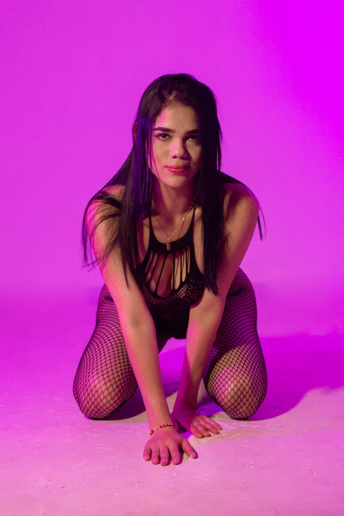 Luna_19 poses with long black hair wearing a red strapless top against a grey curtain background.