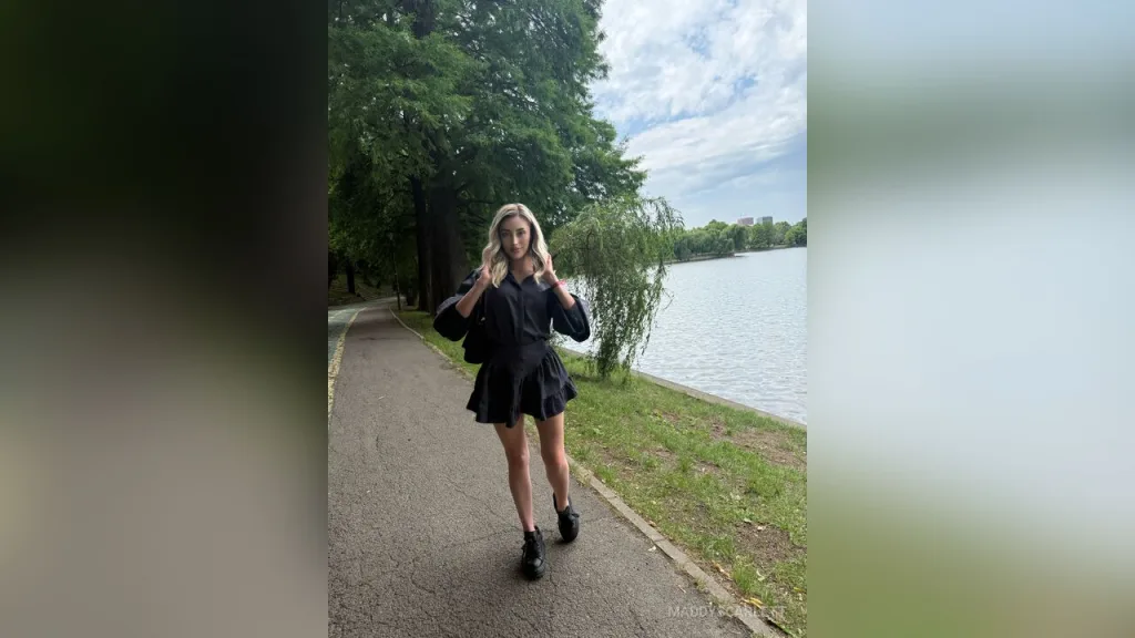 Maddy — MaddyScarlett stands on a paved path next to a lake wearing a short black dress and black boots.