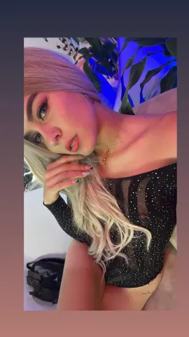 Blonde woman in a black sequin bodysuit relaxing in a room with blue ambient lighting.