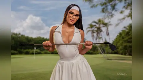 Stylish woman in a white sleeveless dress and headband holding a golf club on a sunny green golf course.