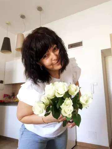 Polunichka039 smiles while holding a large bouquet of white roses in her kitchen.