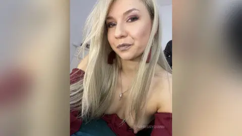 Blonde woman in a maroon off-the-shoulder top posing with a soft, confident expression indoors.