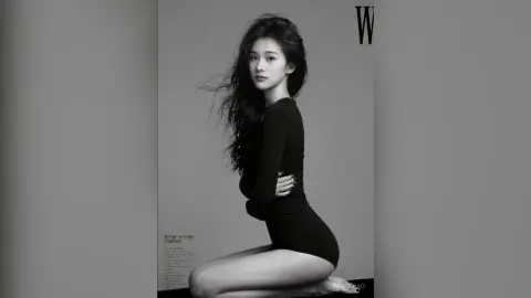 Elegant woman in a black long-sleeve bodysuit posing for a moody black and white fashion studio portrait.