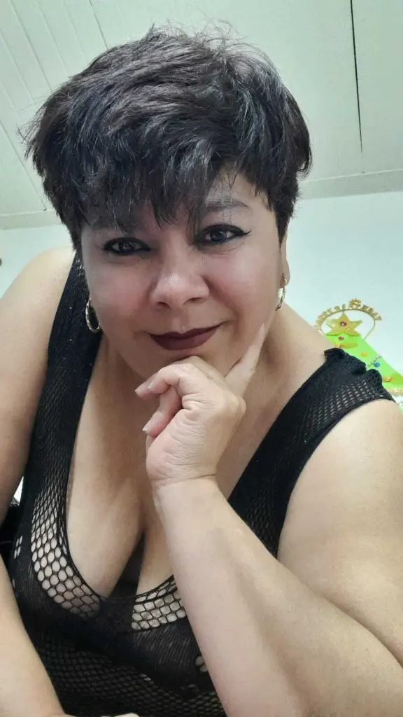 Smiling woman with short dark hair wearing colorful statement jewelry and a black halter top indoors.