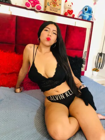 Young woman in black lace lingerie and Calvin Klein underwear relaxing on a bed with red pillows.