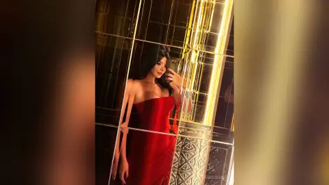Elegant woman in a red strapless evening gown posing in a luxurious gold mirrored room.