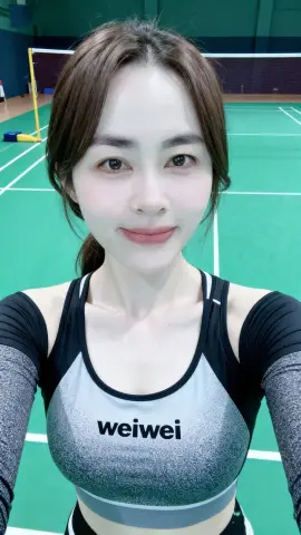 Sweaty woman in black and grey athletic tank top smiling at an indoor green badminton court.
