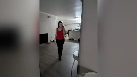 SashaMaroon stands in a room wearing a red tank top and black leggings, holding her phone for a mirror selfie.