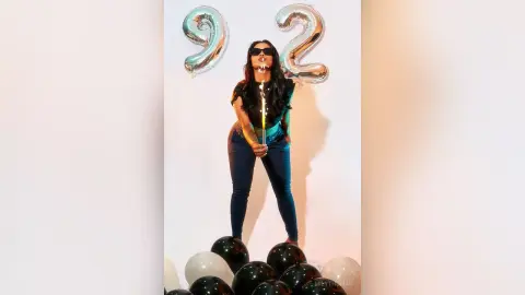 Stylish woman in black top and jeans celebrating a 92nd birthday with silver balloons and festive mood.