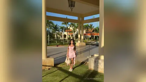 Elegant woman in a pink cocktail dress standing under a sunny outdoor patio veranda.