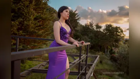 SamanthaHarvey stands on a wooden balcony wearing a purple sequined dress with a deep neckline.