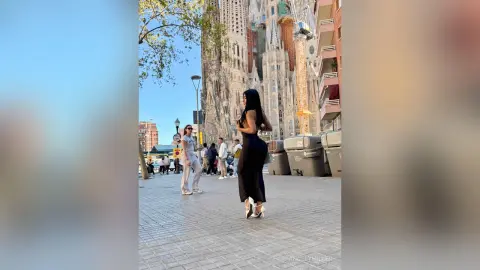 Stylish woman in a black jumpsuit walking through a sunny European city plaza near historic architecture.